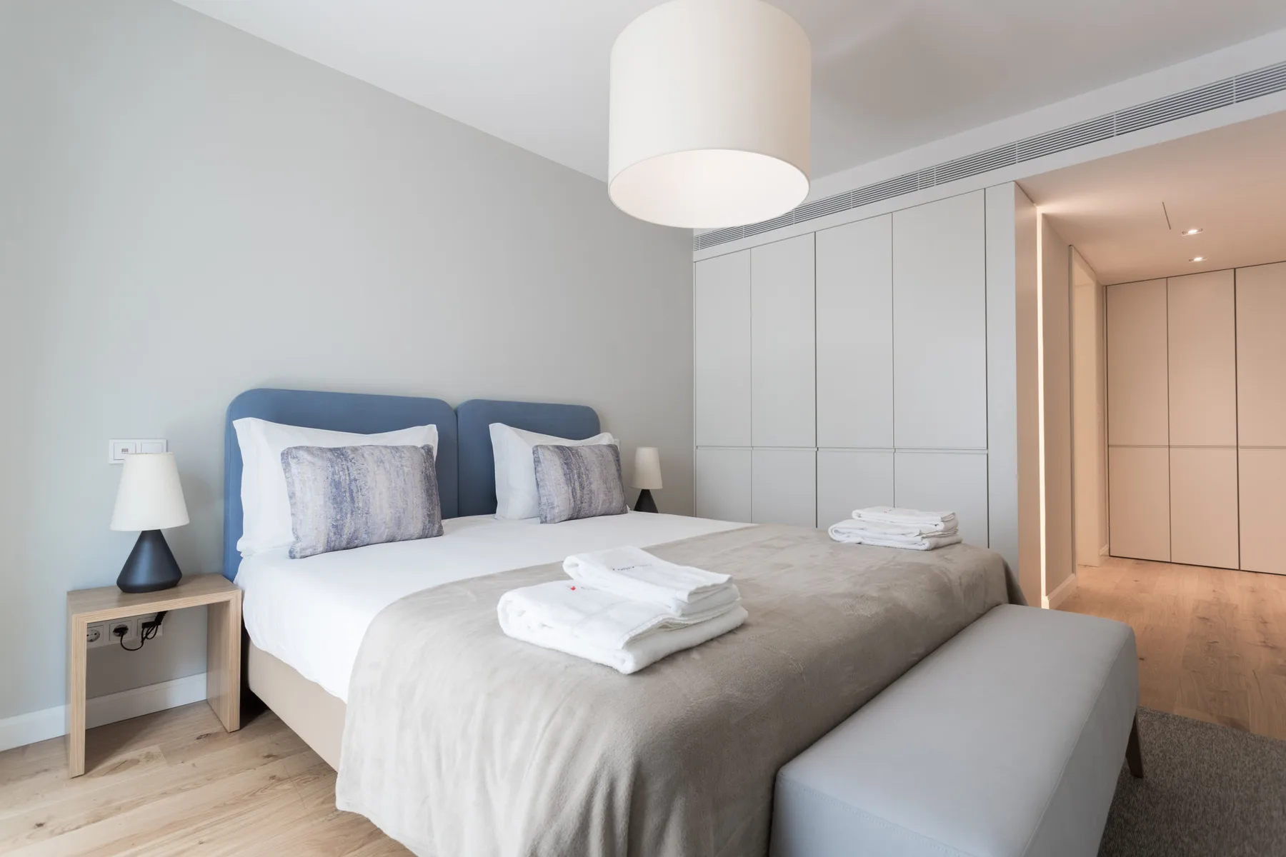A bright bedroom with a neatly made bed and built-in storage.