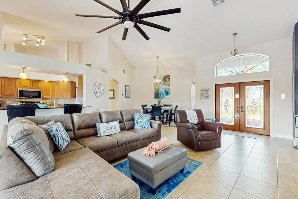 A living room with seating arranged around an ottoman, opening onto a dining area.