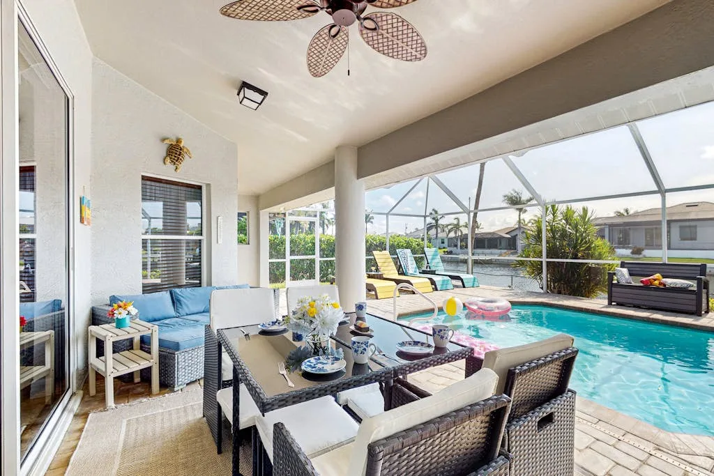 A covered patio with a dining table and seating beside a swimming pool.