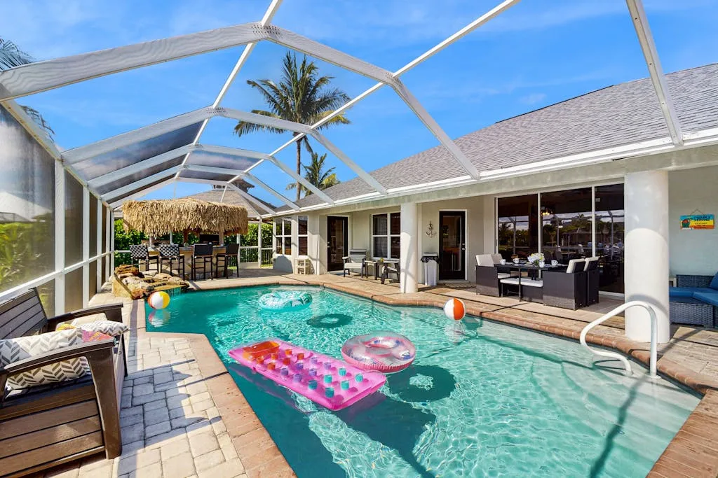 A screened outdoor pool beside a patio with seating and colorful floats.