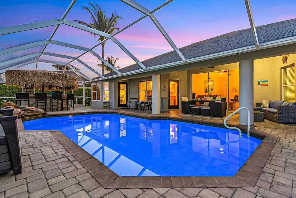 A screened outdoor pool beside a house, with patio seating and a colorful sunset sky.
