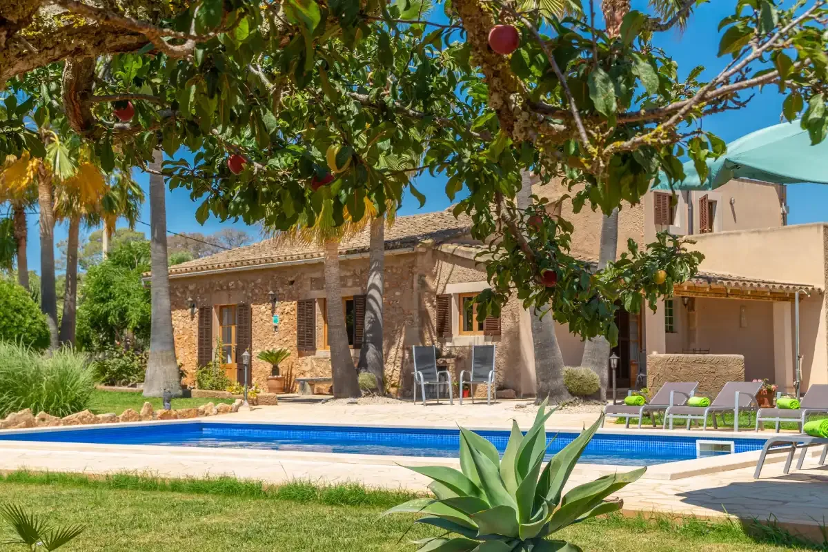 Una casa de piedra da a una piscina en un jardín frondoso.