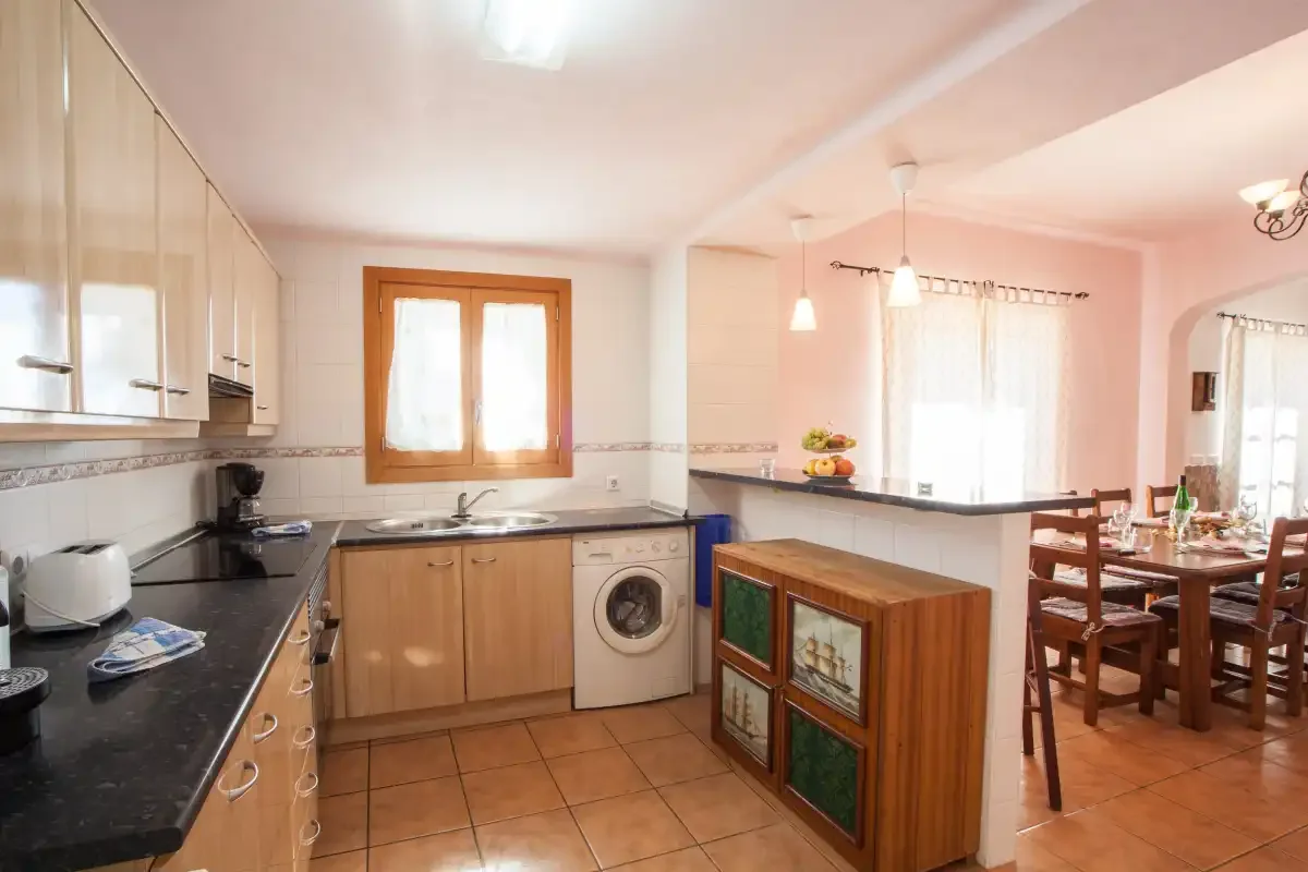 Una cocina con encimeras oscuras se abre a un comedor.