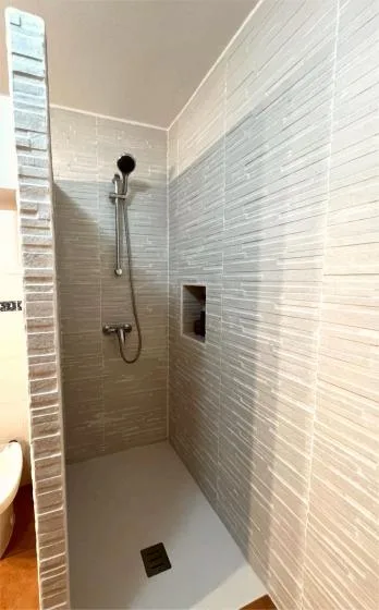 Una zona de ducha alicatada con ducha de mano y desagüe en el suelo.