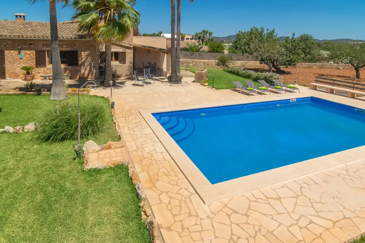 Una piscina junto a un patio de piedra y un jardín cuidado.