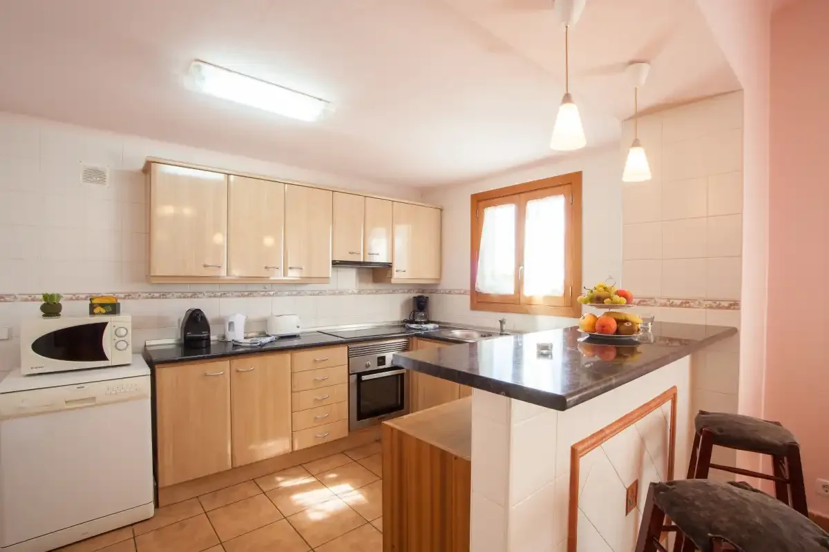 Una cocina luminosa con gabinetes de madera clara y una encimera central.