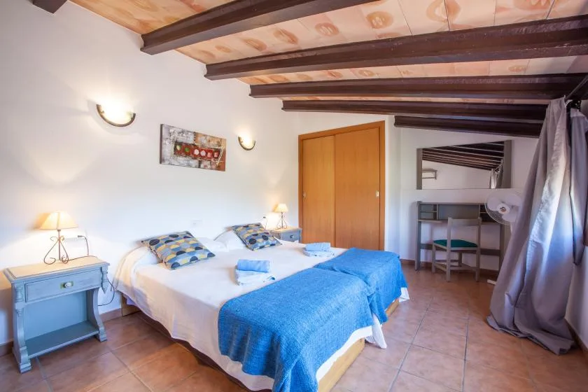Un dormitorio con dos camas, ropa de cama azul y vigas de techo a la vista.
