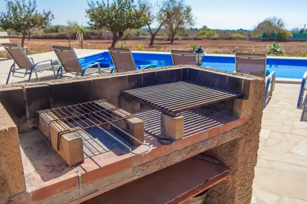Una parrilla exterior está junto a una piscina y asientos de patio.