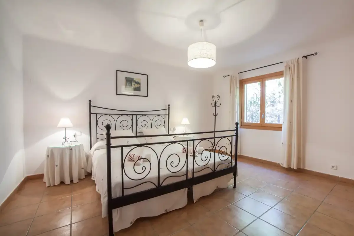 Un dormitorio con una cama de metal negro, mesillas y una ventana.