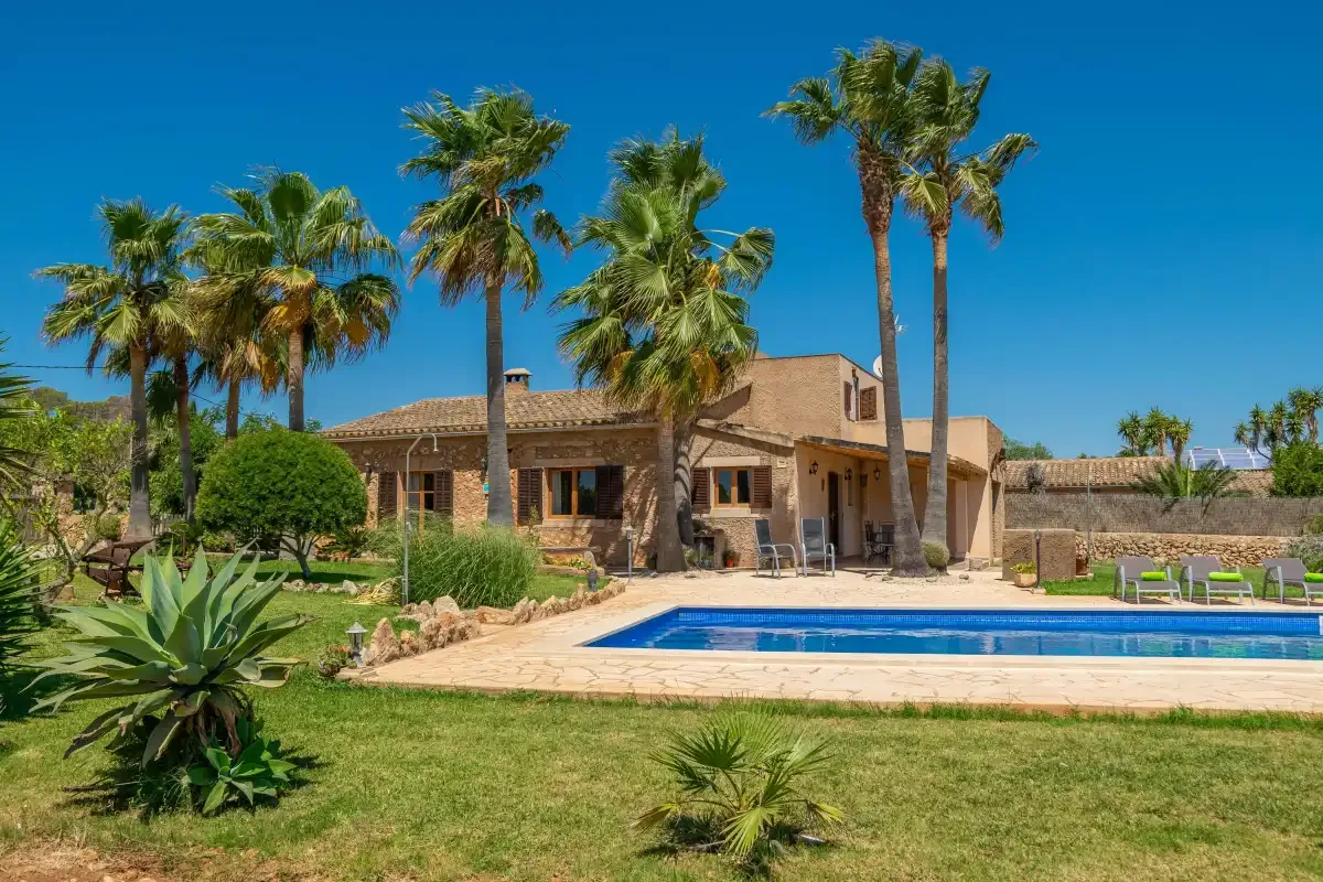 Una casa y una piscina están rodeadas de palmeras y jardines.