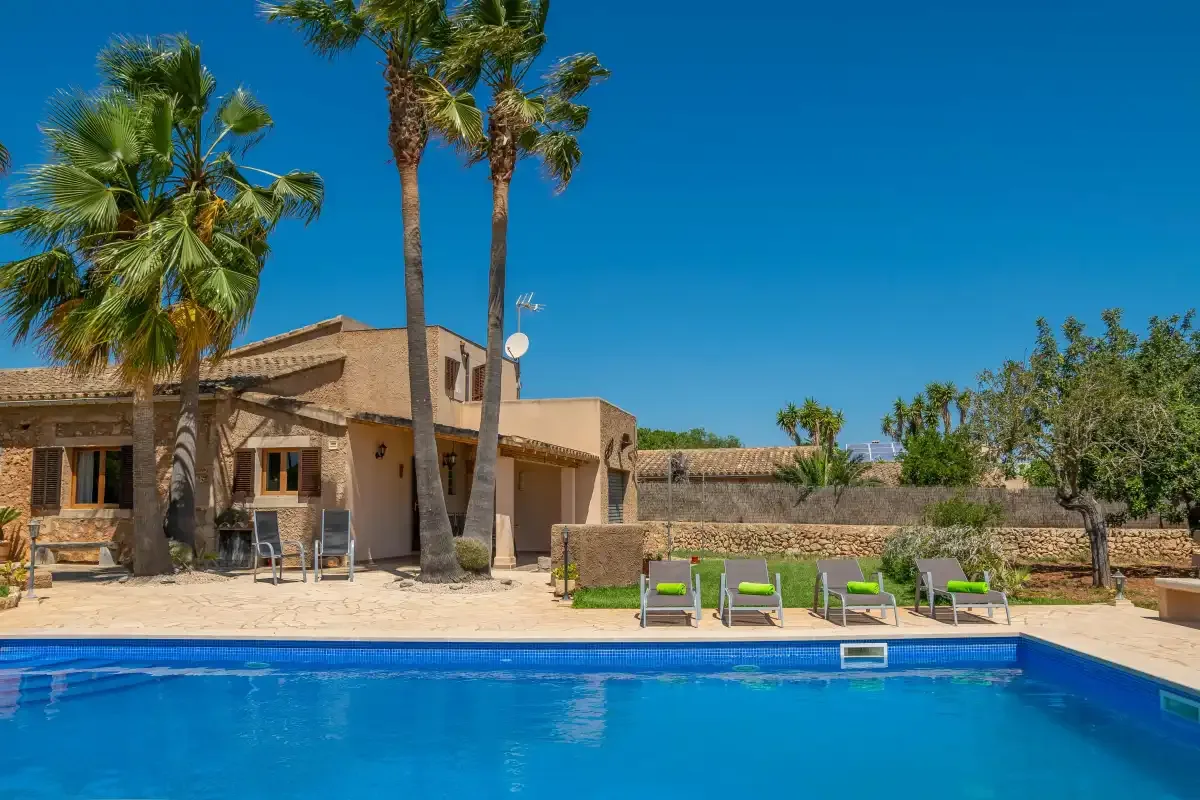 Una piscina está frente a una casa de piedra y palmeras.