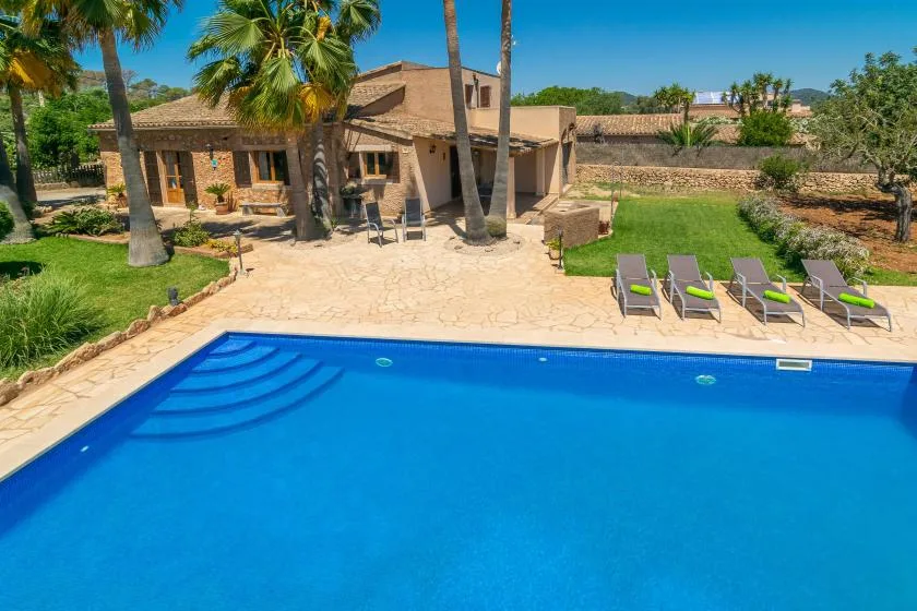 Una piscina al aire libre está junto a un patio pavimentado y jardines.