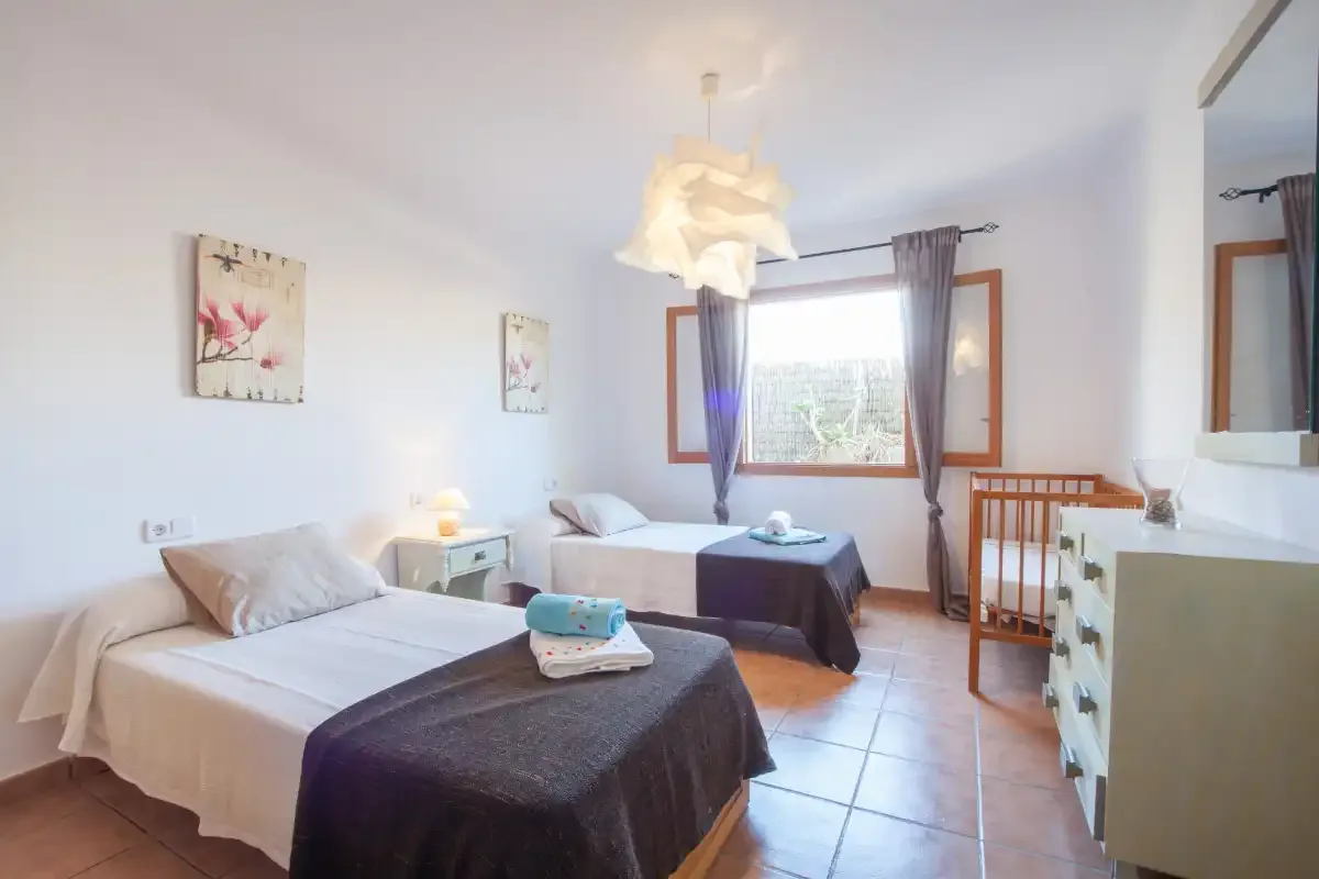 Un dormitorio luminoso con dos camas y una ventana con vistas a la vegetación.