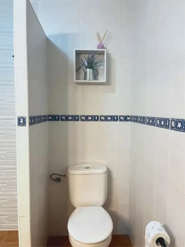 Un baño alicatado con un inodoro y una pequeña repisa en la pared.