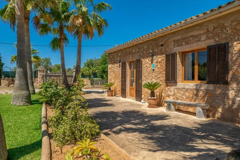 Un edificio de piedra da a una zona exterior pavimentada con palmeras y vegetación.