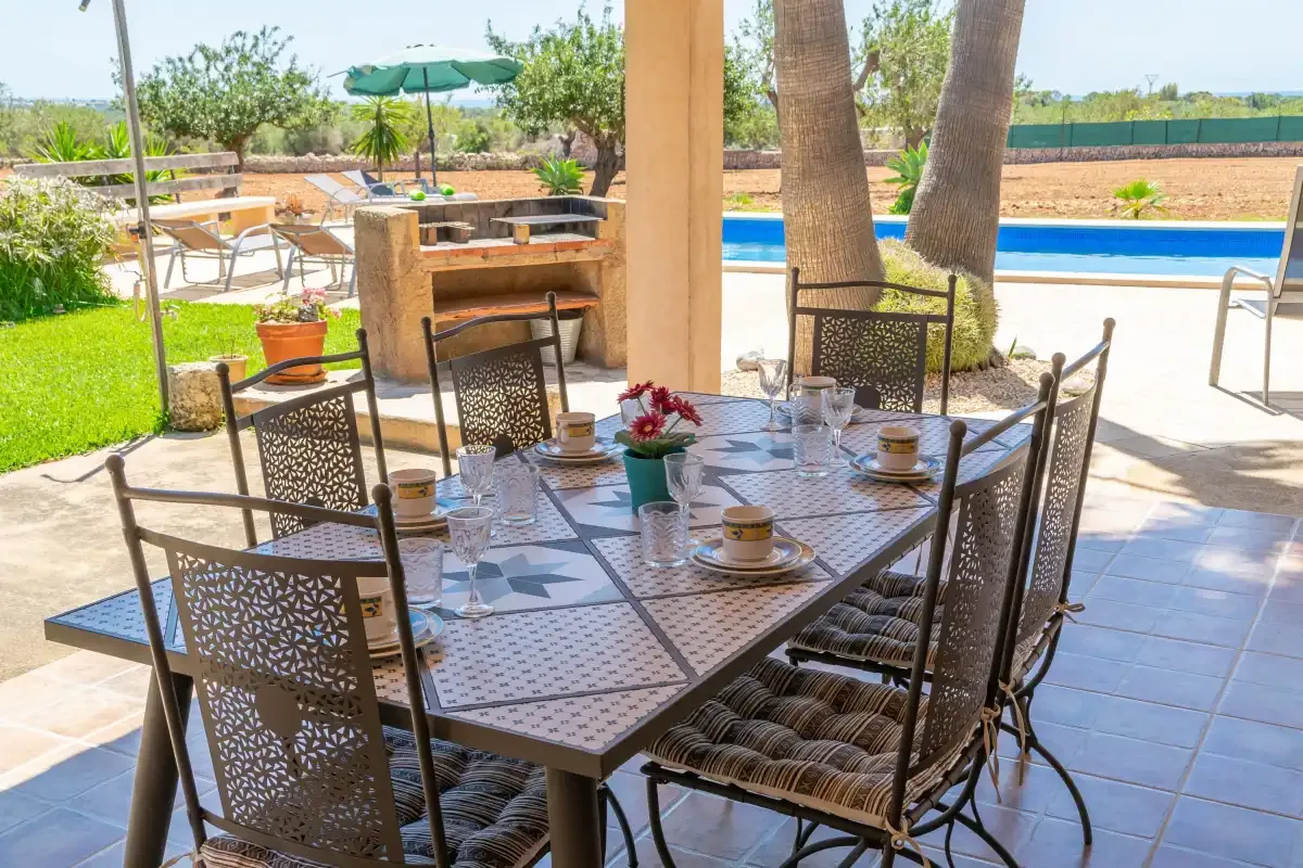 Una mesa de comedor al aire libre con platos está junto a una piscina.