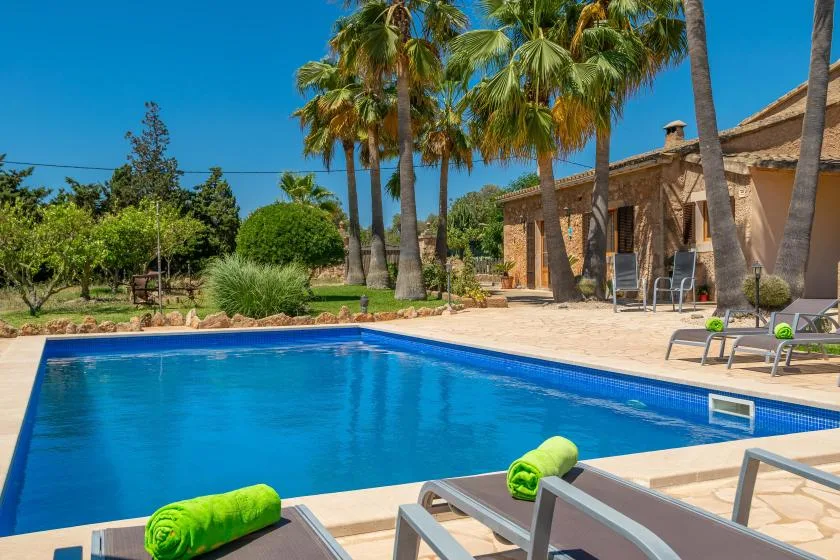 Una piscina junto a un patio soleado y un edificio de piedra.
