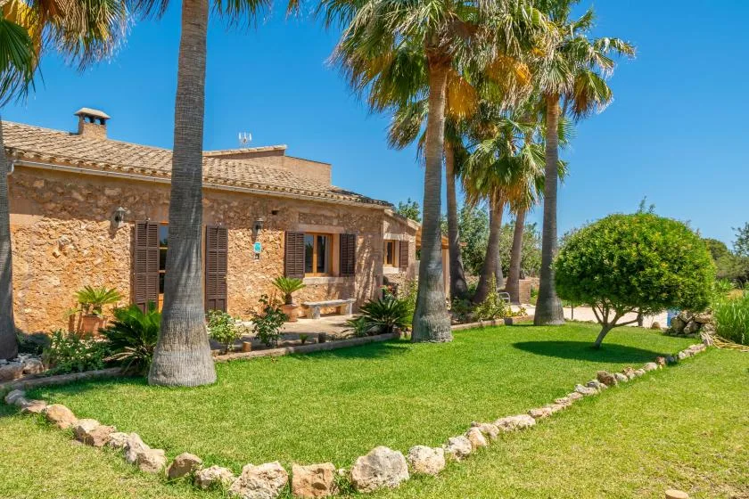 Una casa de piedra se encuentra junto a un césped verde y palmeras.