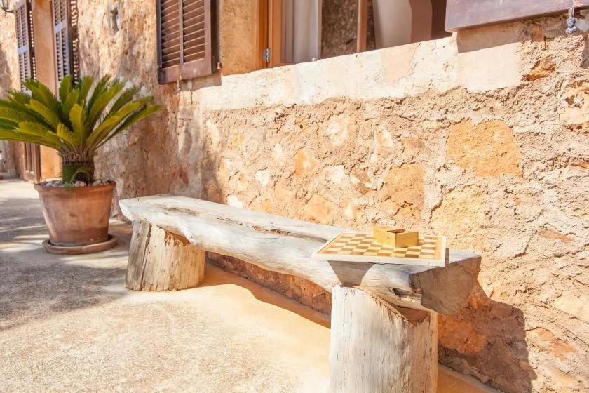 Un banco con un pequeño juego de mesa está junto a un muro de piedra en un pasaje soleado.