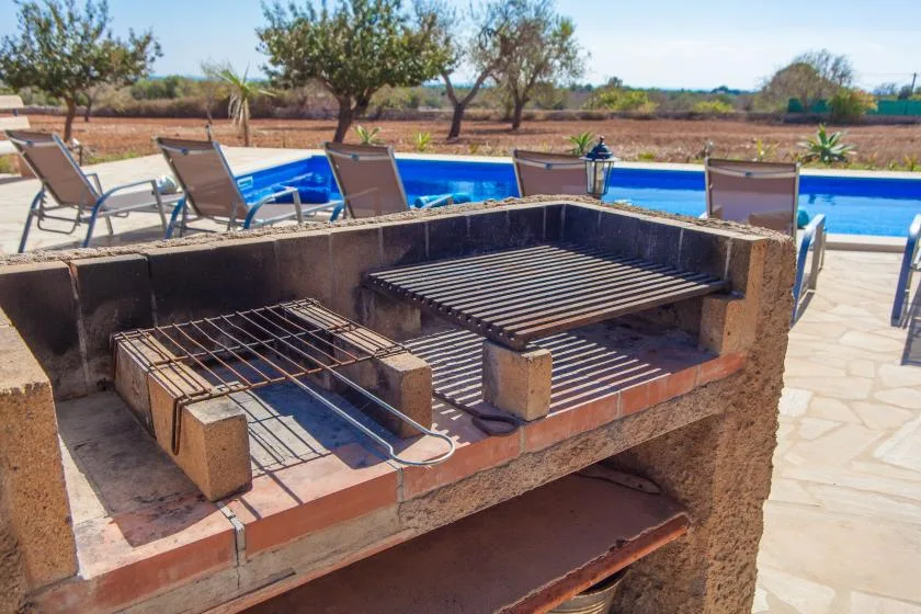 Una parrilla al aire libre está junto a una piscina y asientos de patio.