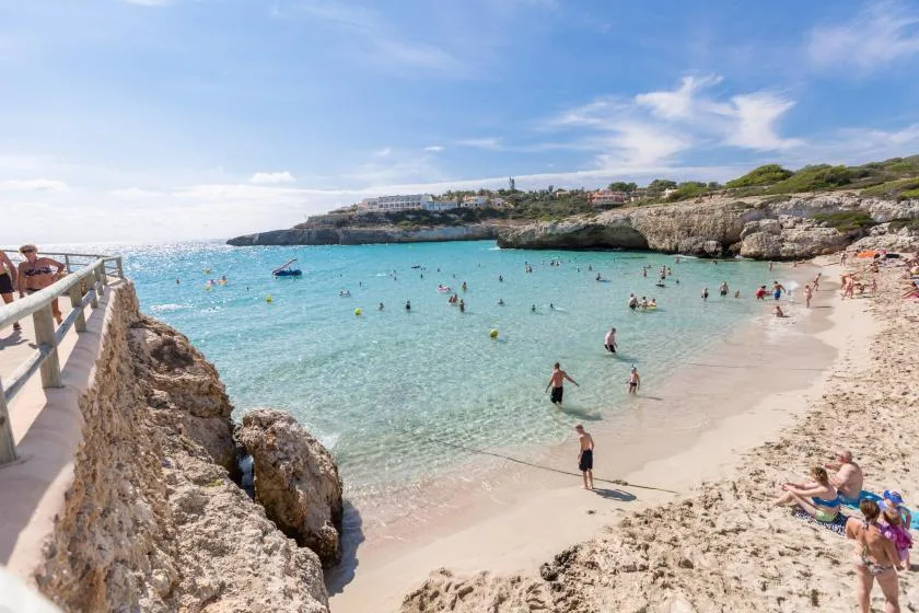 Una cala soleada con agua turquesa clara, bañistas y una costa rocosa.