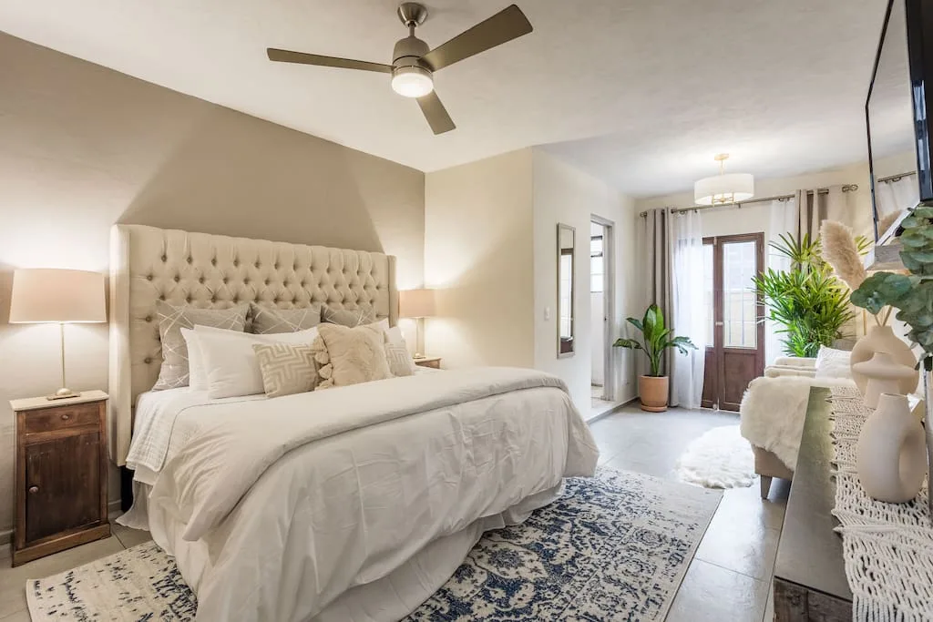 A bedroom with a tufted headboard, ceiling fan, and bright sitting area.