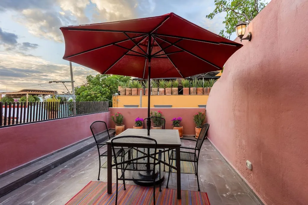Rooftop terrace with dining table, red umbrella, and potted plants overlooking the town