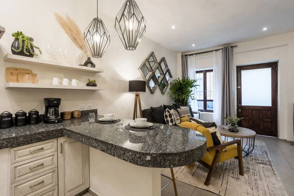 Open kitchen and dining area with granite countertop, floating shelves, and geometric pendant lights
