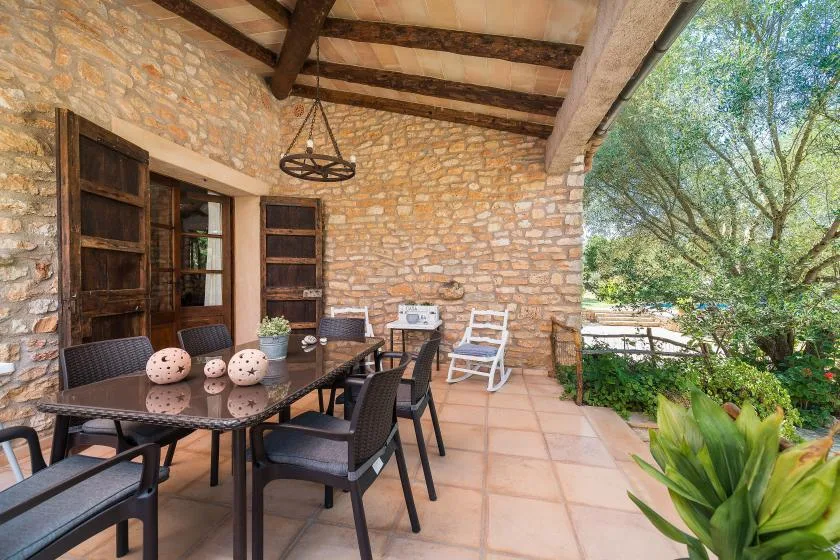 A covered outdoor dining area with a table and seating beside a stone wall.