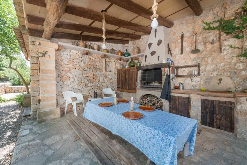 A rustic stone outdoor kitchen with a blue-covered table and built-in oven.