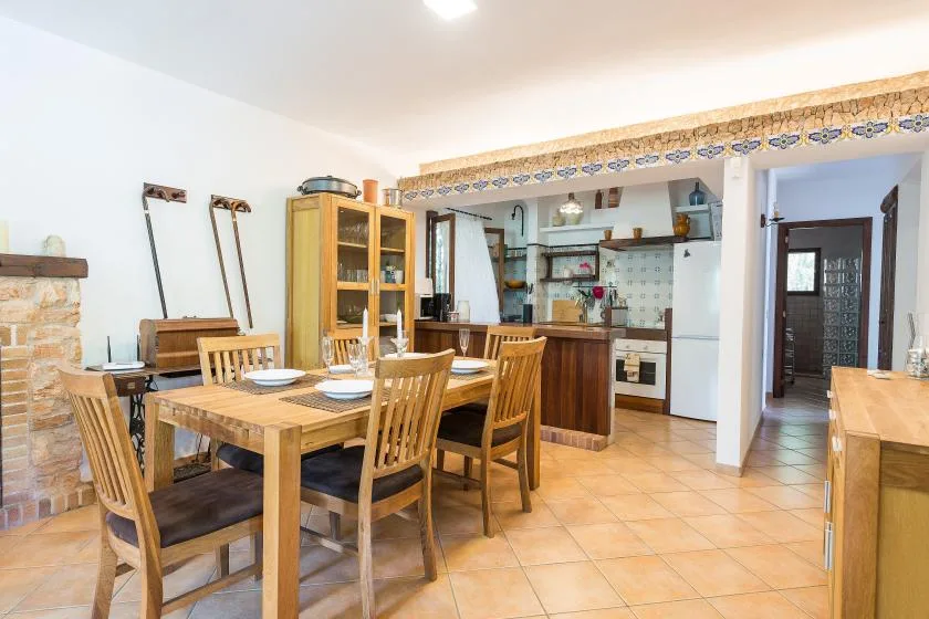 A dining area with a wooden table and an open kitchen in the background.