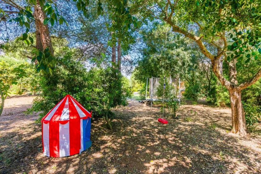 A shaded garden with a small red-and-white striped play tent beneath the trees.