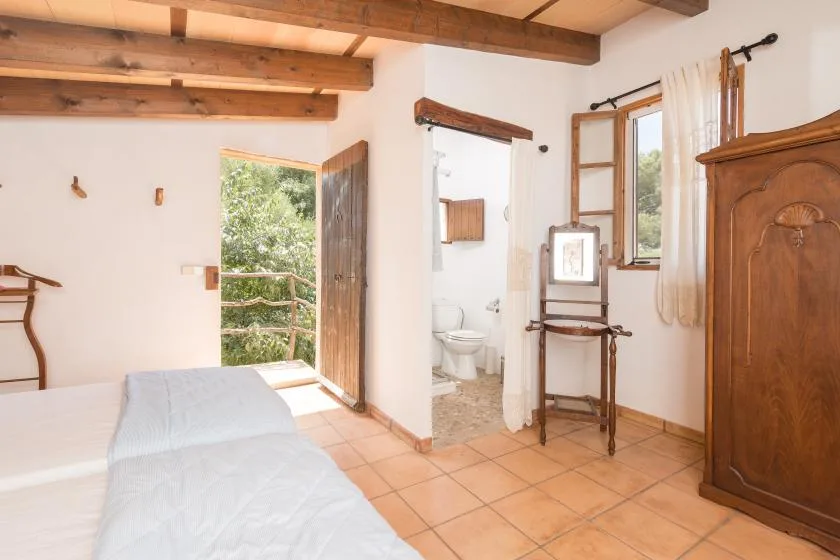 A bedroom with an open doorway leading to a small bathroom and a leafy outdoor view.