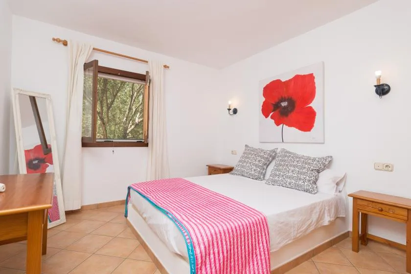 A bedroom with a bed, patterned pillows, and a red flower painting.