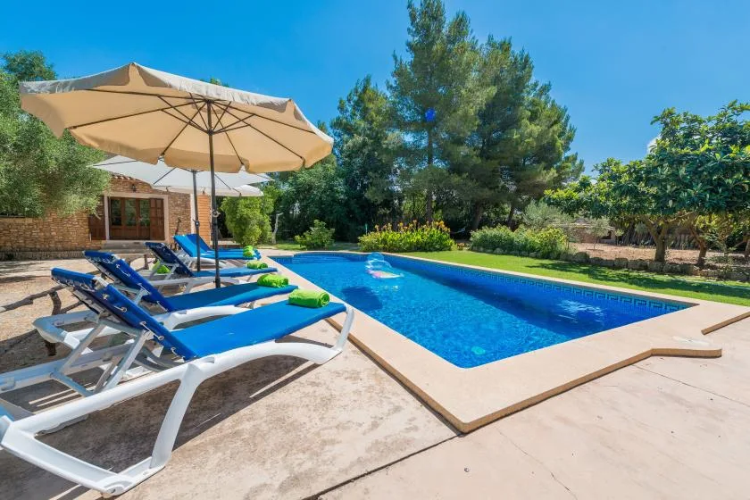 An outdoor swimming pool with blue loungers and a large shade umbrella.
