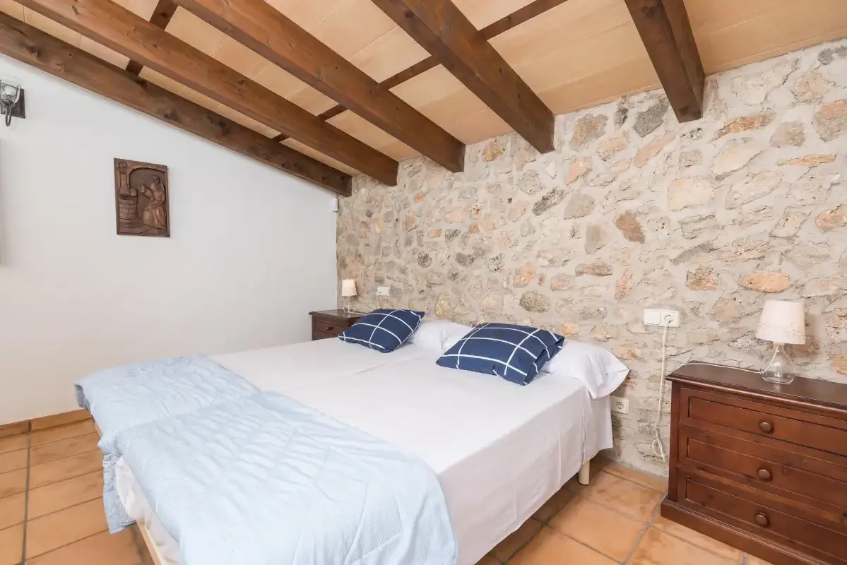 A bedroom with a double bed, blue pillows, and exposed wooden ceiling beams.