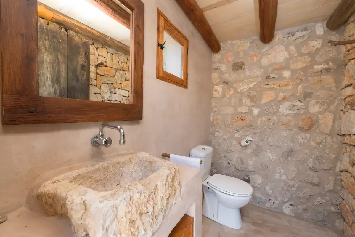 A rustic bathroom with a stone sink, toilet, and exposed ceiling beams.