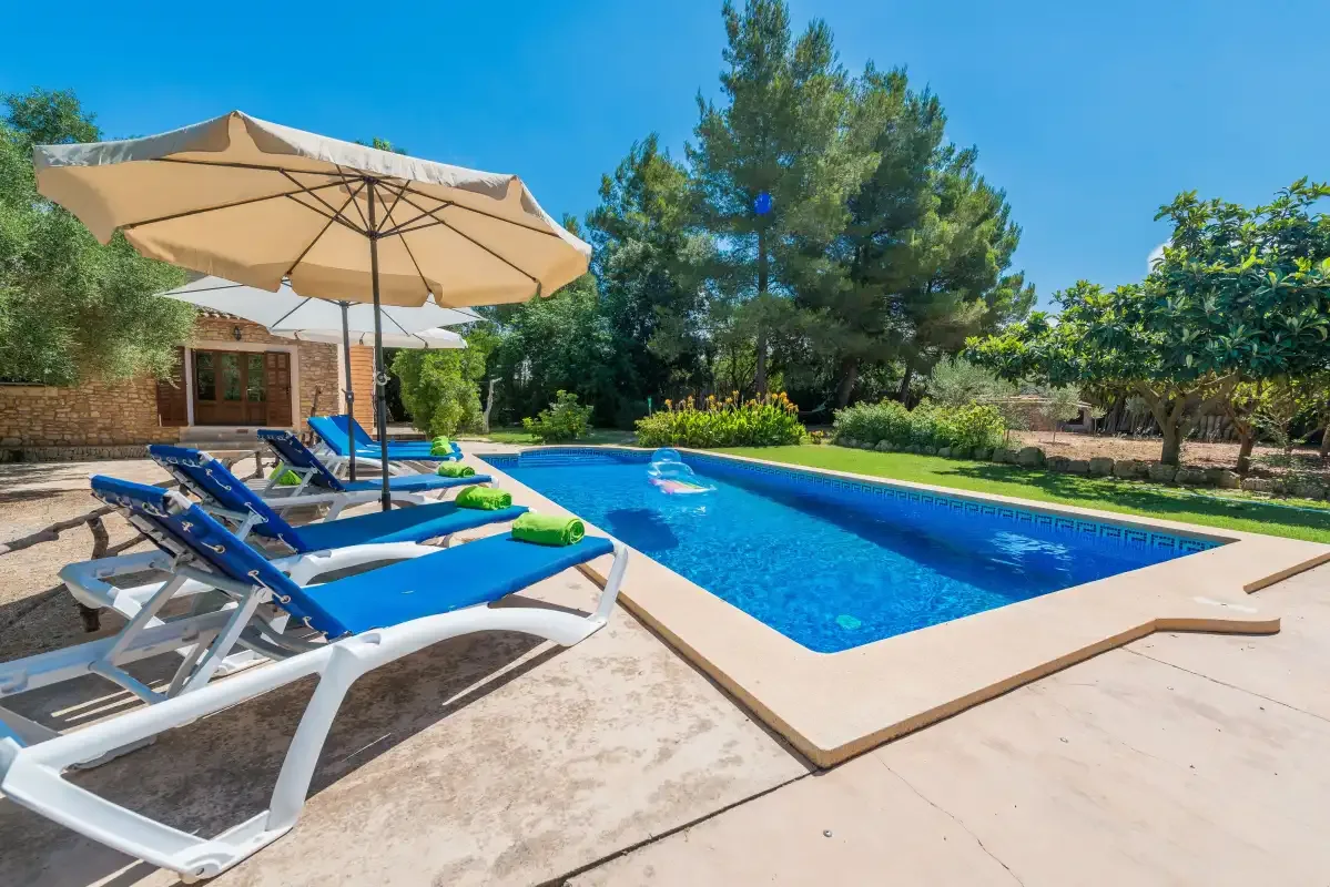 An outdoor swimming pool bordered by blue sun loungers and a large umbrella.