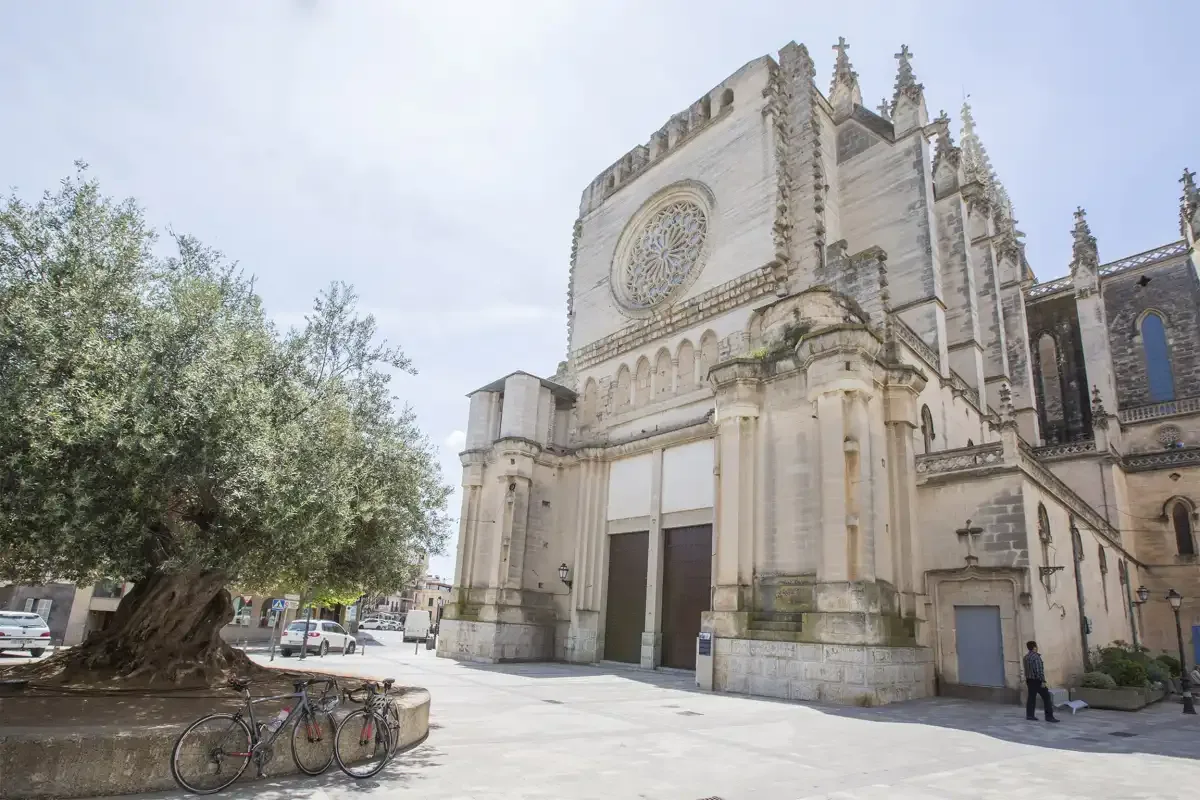 A large stone church with a circular window stands beside a tree-lined plaza.