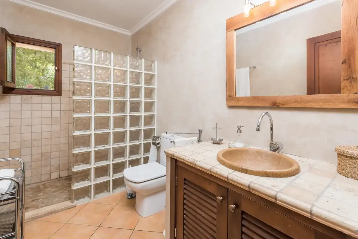 A tiled bathroom with a sink, toilet, and glass-block partition.