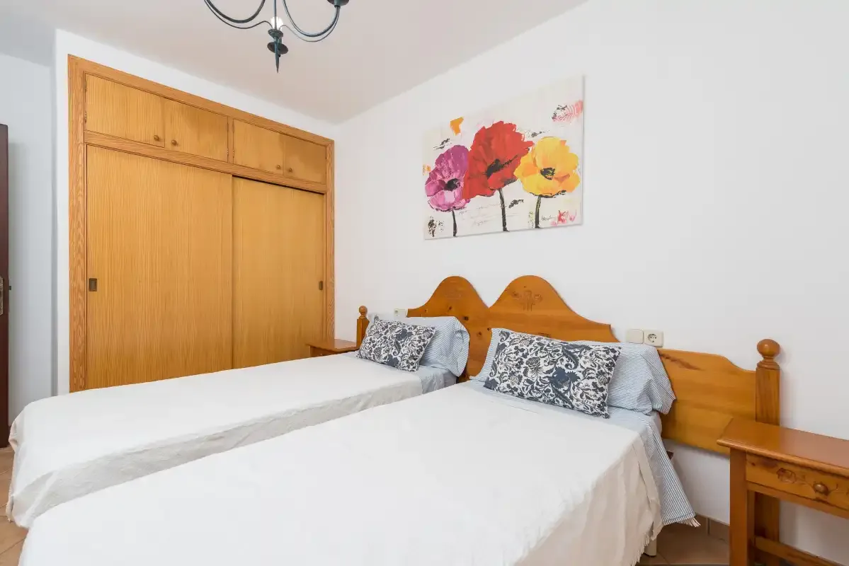 A bedroom with two beds, wooden wardrobes, and colorful floral artwork.