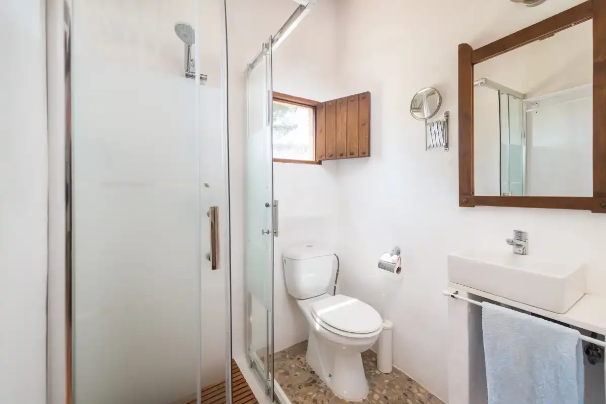 A bright bathroom with a shower, toilet, and sink beneath a wall mirror.