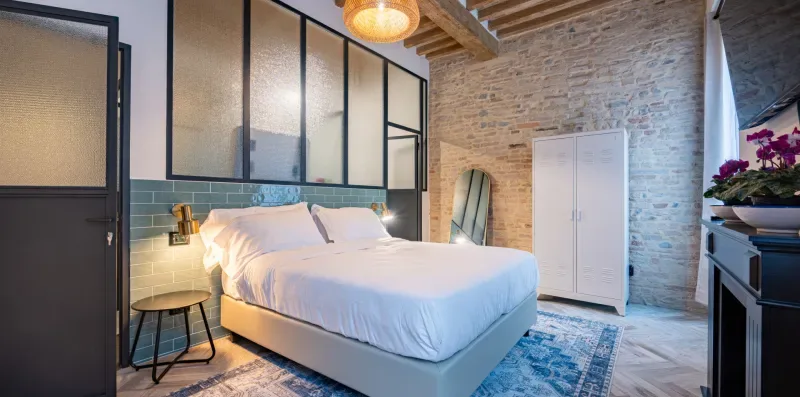 Un dormitorio con una cama blanca, una mesa de noche y una pared de piedra vista.