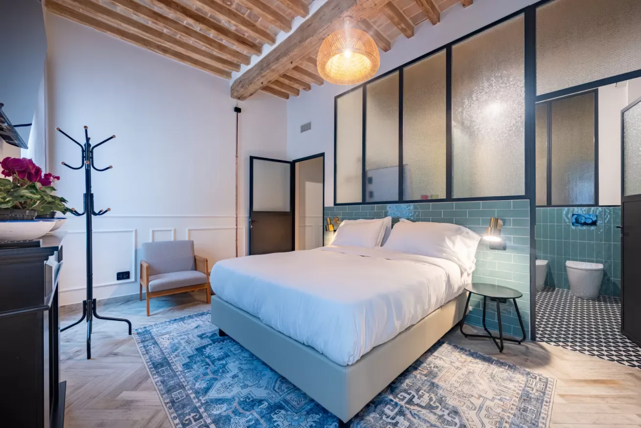Un dormitorio con una cama bien hecha y un baño con mamparas de vidrio.