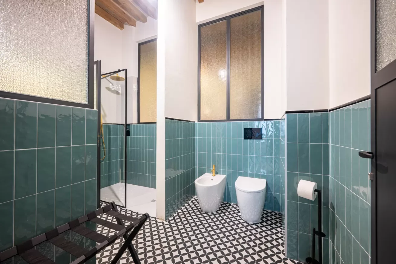 Un baño alicatado con una ducha y dos inodoros.