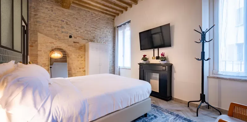 Un dormitorio con una cama blanca, una pared de ladrillo visto y un televisor en la pared.