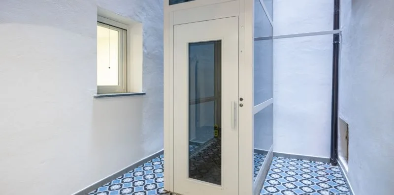 Un baño con suelo de baldosas, una ducha de cristal y una ventana estrecha.