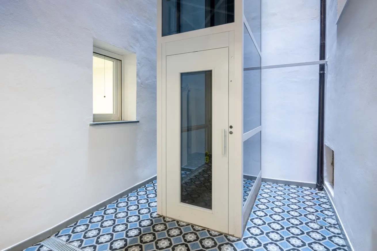 Una puerta blanca de entrada está en un espacio estrecho con suelo de baldosas estampadas.