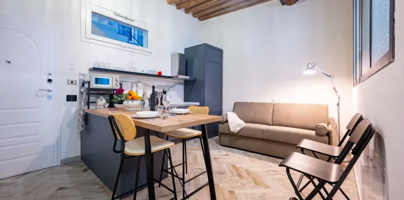 Una pequeña zona de estar y comedor con mesa, asientos y cocina.