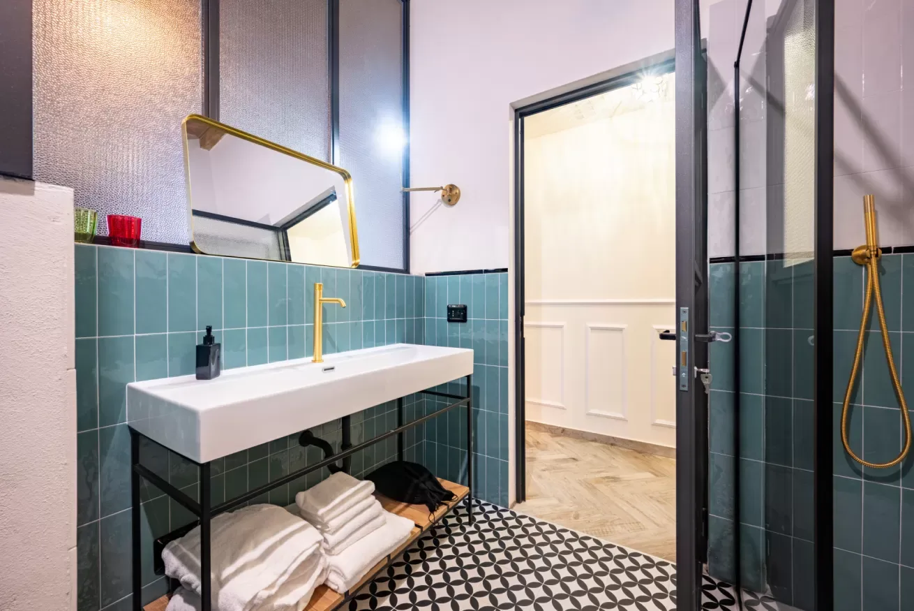 Un baño con lavabo de pared, paredes alicatadas y una ducha con mampara de vidrio.